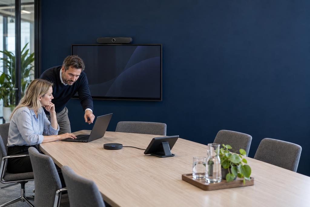 Illustratieve Microsoft 365-trainer en medewerker die deelnemen, camera, microfoon, roomcontroller en schermdeling in een hybride Teams-vergadering oefenen