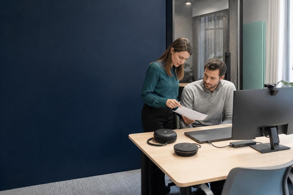 Illustratieve medewerker en ICT-specialist die monitor, camera, audio, dock en Microsoft Teams op een hybride werkplek testen tijdens het inrichten van een werkplek